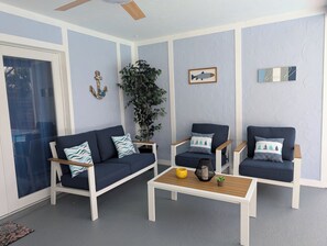 Huoneessa on sininen sohva, kaksi nojatuolia, sohvapöytä ja ruukussa oleva kasvi.