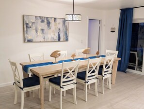 Un coin repas avec une table en bois, des chaises blanches, un chemin de table bleu et un luminaire suspendu.