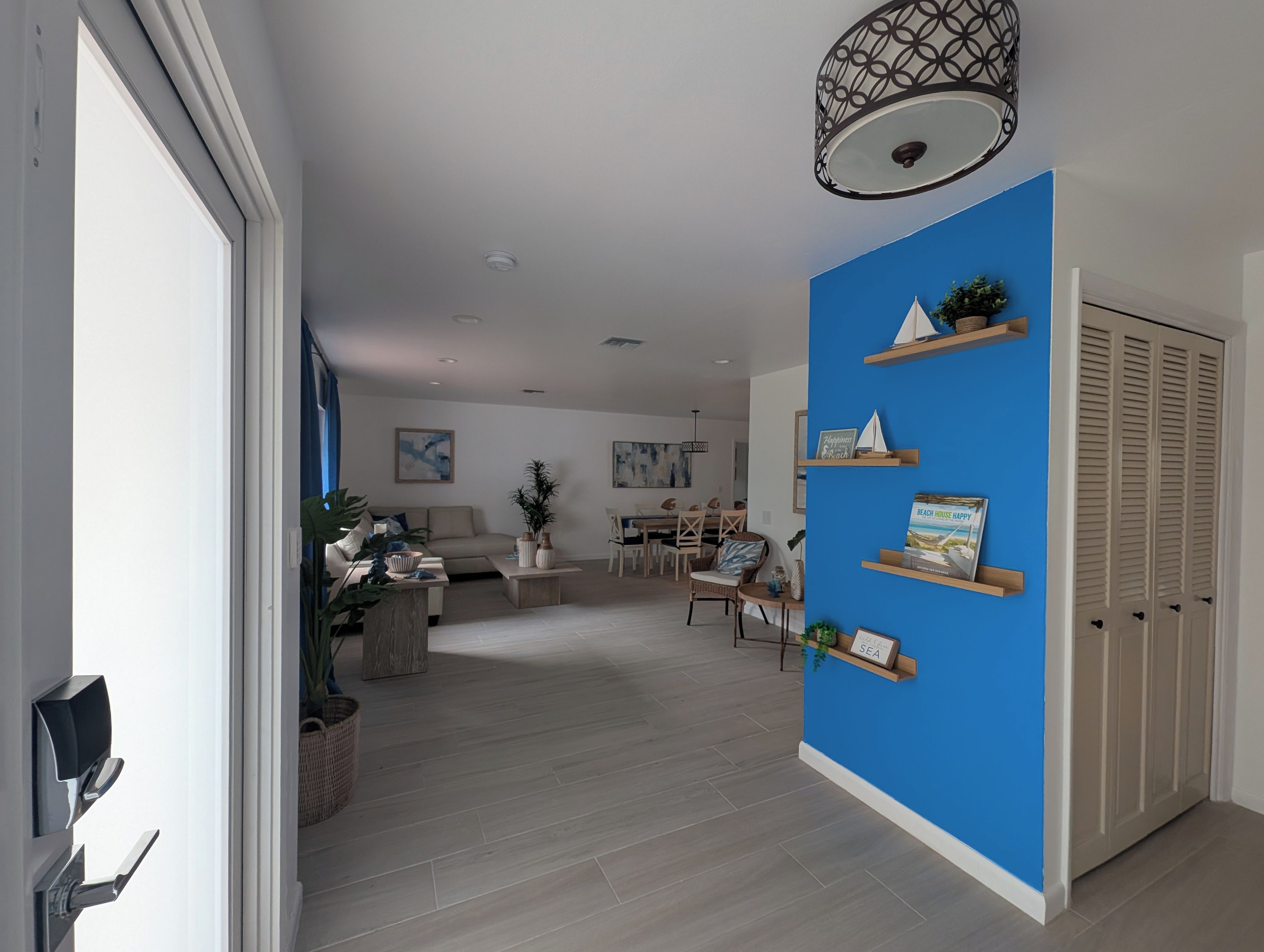 A modern living room with a blue accent wall, wooden flooring, and a dining area in the background.