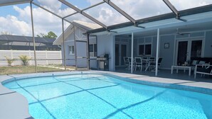 A swimming pool with a glass enclosure, a patio area with outdoor furniture, and a covered seating area. - Siesta Breeze (Sarasota)