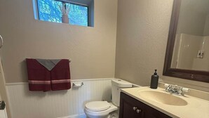 A bathroom with a toilet, sink, mirror, and a window above the toilet.
