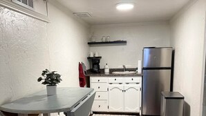 A compact kitchen with white cabinets, a stainless steel refrigerator, a coffee maker, and a potted plant.