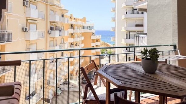 Ein Balkon mit Tisch und Stühlen, mit Blick auf eine Küstenlandschaft mit mehrstöckigen Gebäuden.