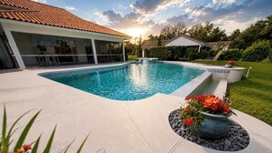 Una piscina de borde curvo, un porche cubierto y una jardinera con flores rojas.