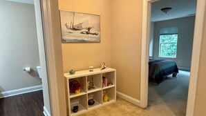 A hallway with a white console table, a painting of a sailboat, and a bedroom with a bed and window. - Pet friendly 3-bedroom townhome walking distance to charming downtown Aiken (Aiken)