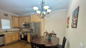 A kitchen with wooden cabinets, a stainless steel refrigerator, a microwave, and a dishwasher. There is a dining table with chairs and a chandelier above. - Pet friendly 3-bedroom townhome walking distance to charming downtown Aiken (Aiken)
