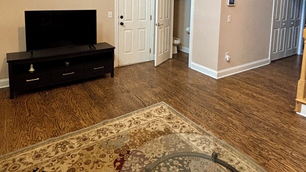 A spacious living area with hardwood flooring, a flat-screen TV on a black entertainment unit, a patterned rug, and a glass coffee table. - Pet friendly 3-bedroom townhome walking distance to charming downtown Aiken (Aiken)