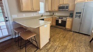 A kitchen with wooden cabinets, a stainless steel refrigerator, a microwave, and an oven. There are two bar stools and a window with blinds. - Pet friendly 3-bedroom townhome walking distance to charming downtown Aiken (Aiken)