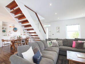 Ein modernes Wohnzimmer mit Treppe, grauen Sofas und einem Essbereich.
