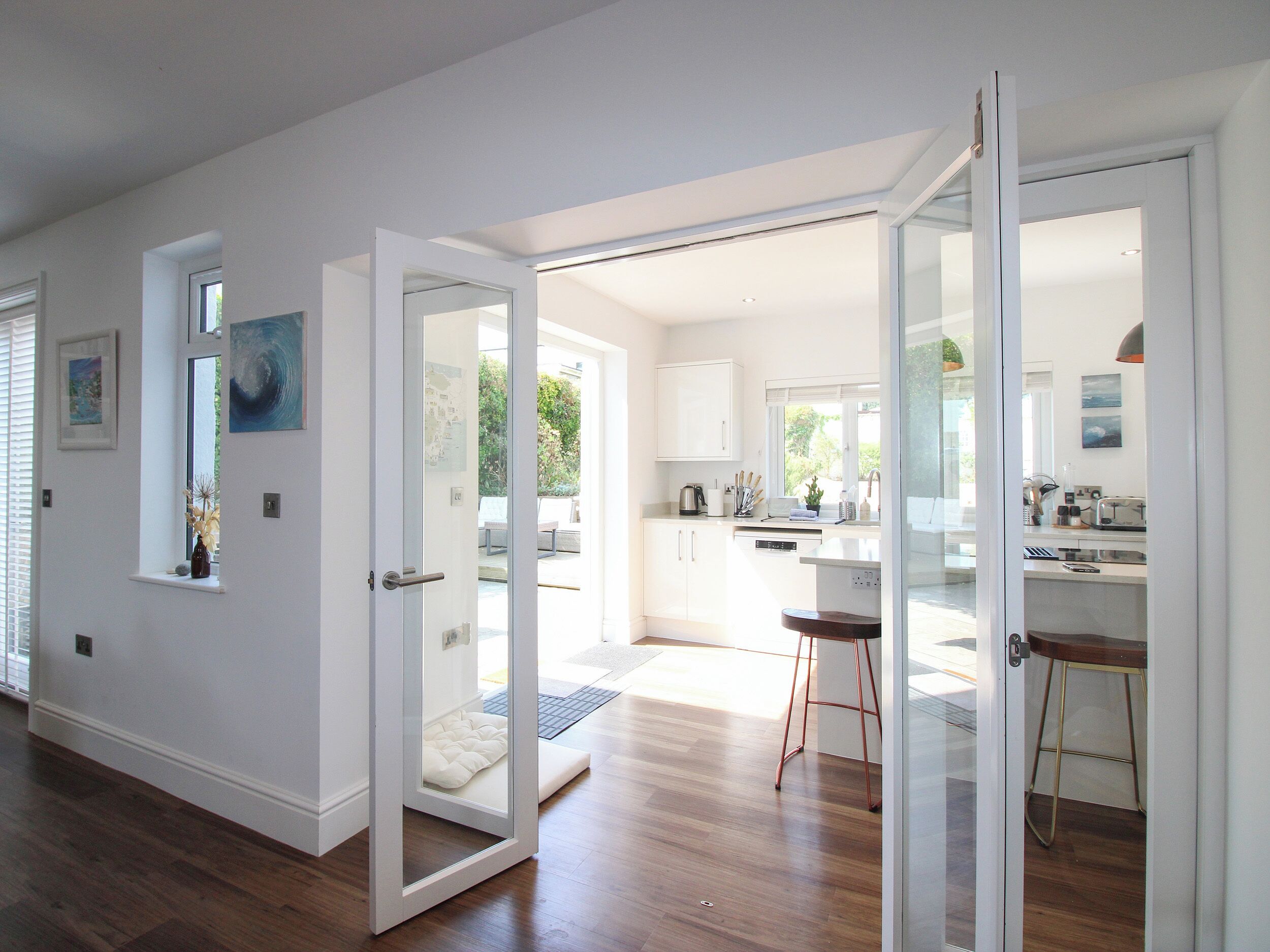 A modern kitchen with white cabinets, a dining area with stools, and a sliding glass door leading to a patio.