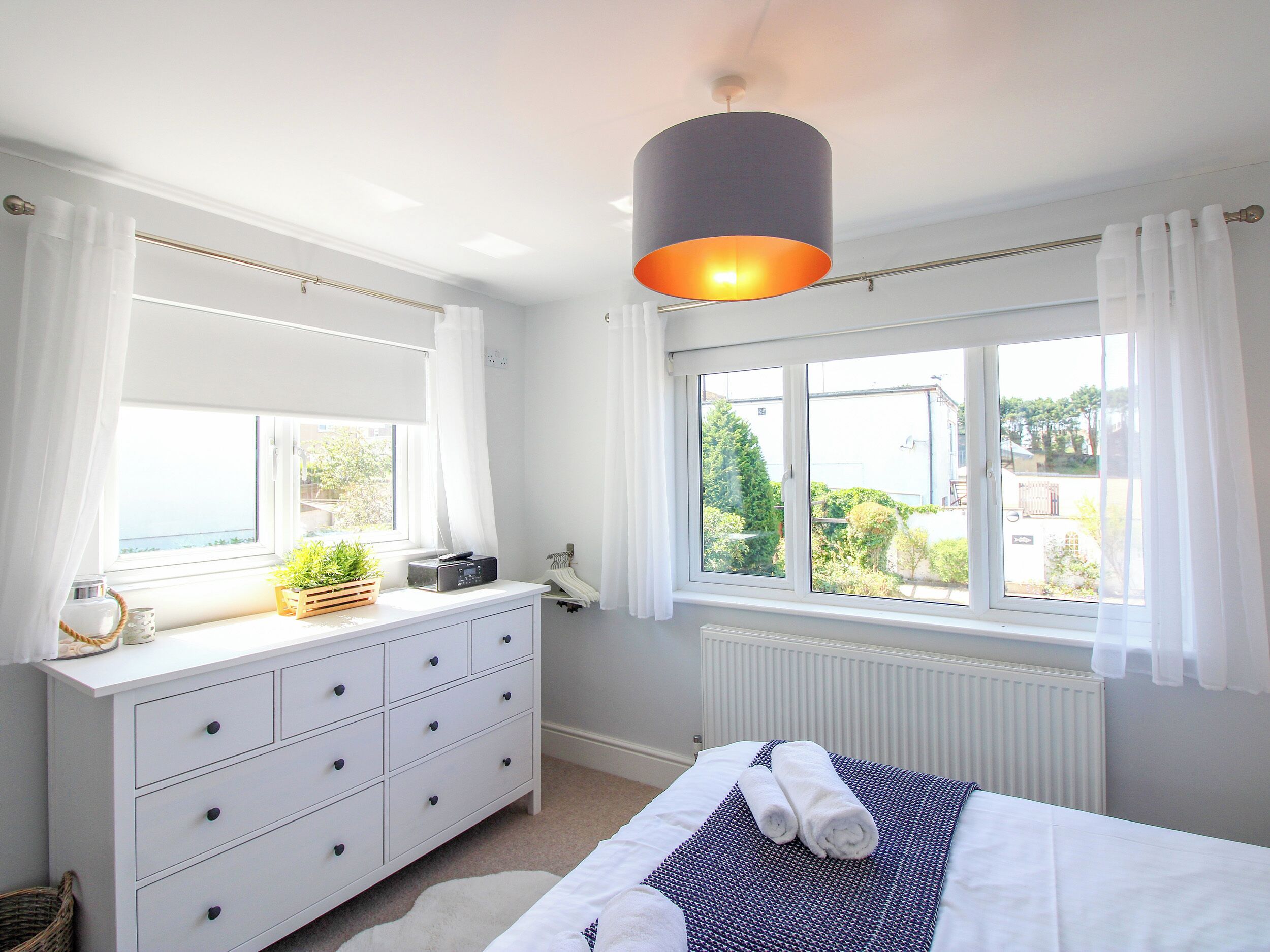 A bedroom with a bed, dresser, window, and a hanging light fixture.
