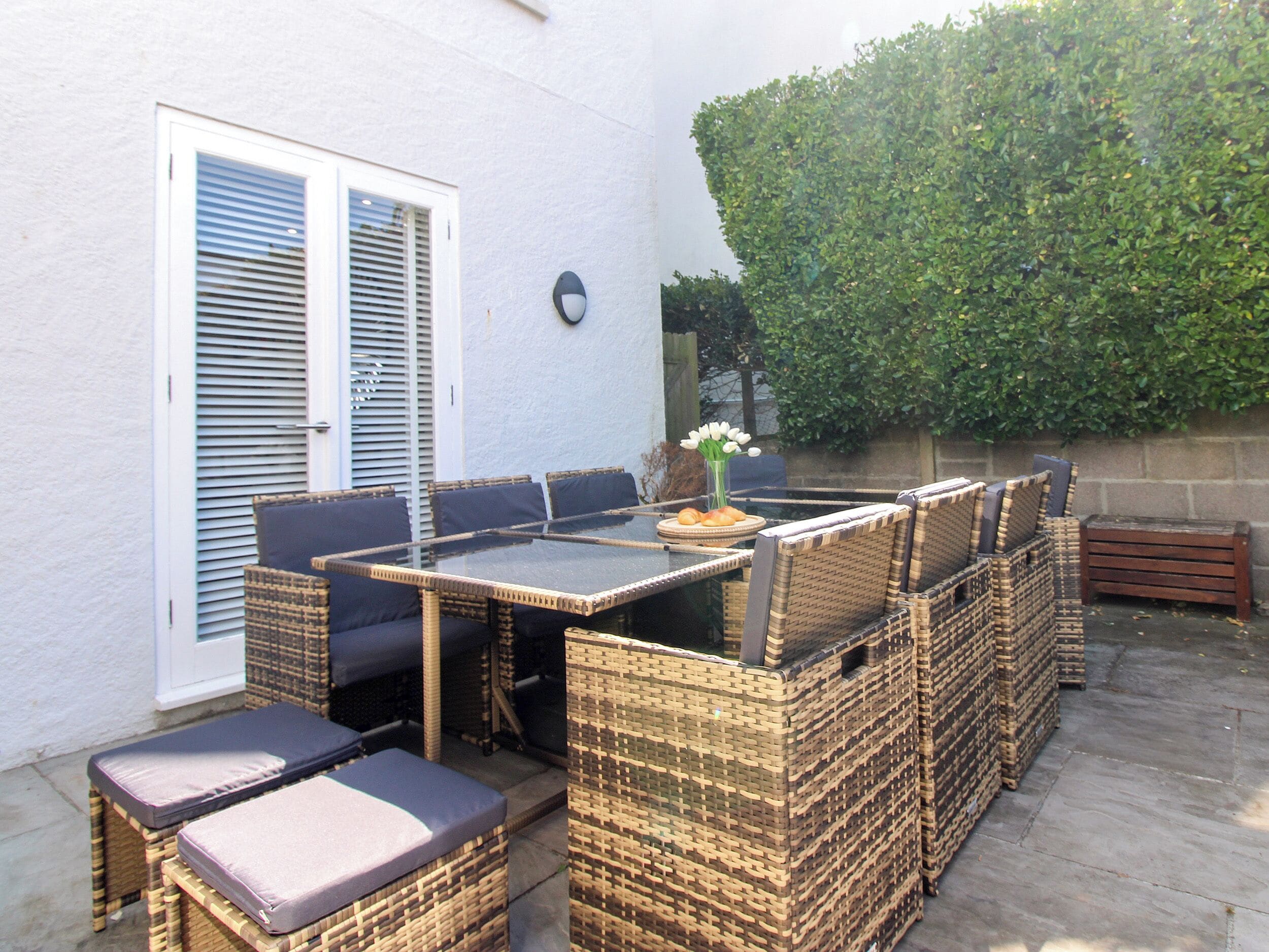 An outdoor patio with a glass-top table surrounded by wicker chairs and cushions.