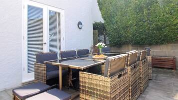 Un patio al aire libre con una mesa de vidrio rodeada de sillas y cojines de mimbre.