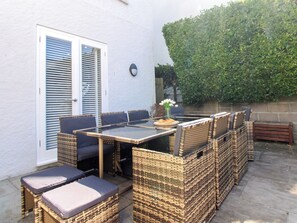 An outdoor patio with a glass-top table surrounded by wicker chairs and cushions. - Lorrell (Salcombe)