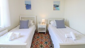 Ein Schlafzimmer mit zwei Betten, einem Nachttisch mit Lampe und einem farbenfrohen Teppich.