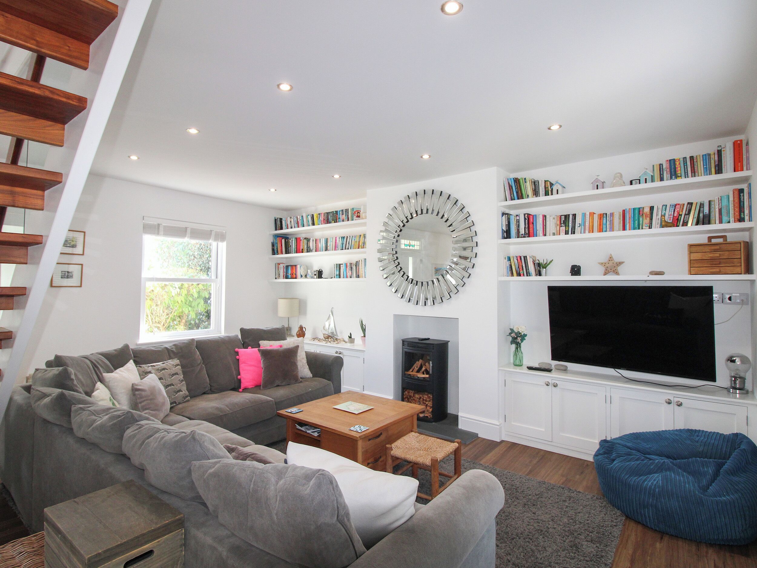 A modern living room with a grey sofa, a blue bean bag, a fireplace, and a bookshelf filled with books.
