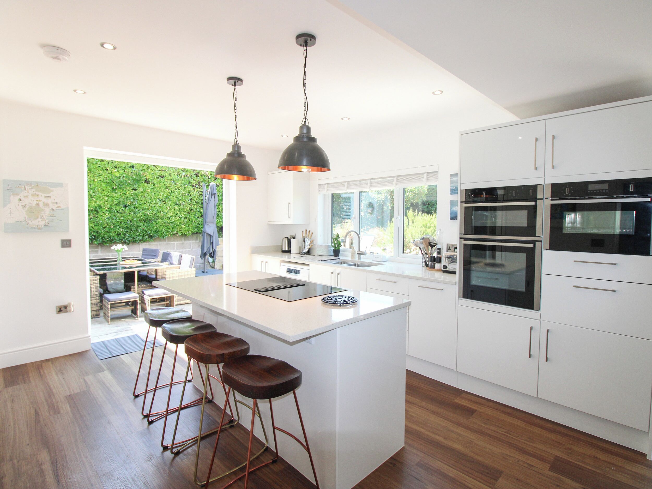 Een moderne keuken met witte kasten, roestvrijstalen apparatuur en een centraal kookeiland met barstoelen.