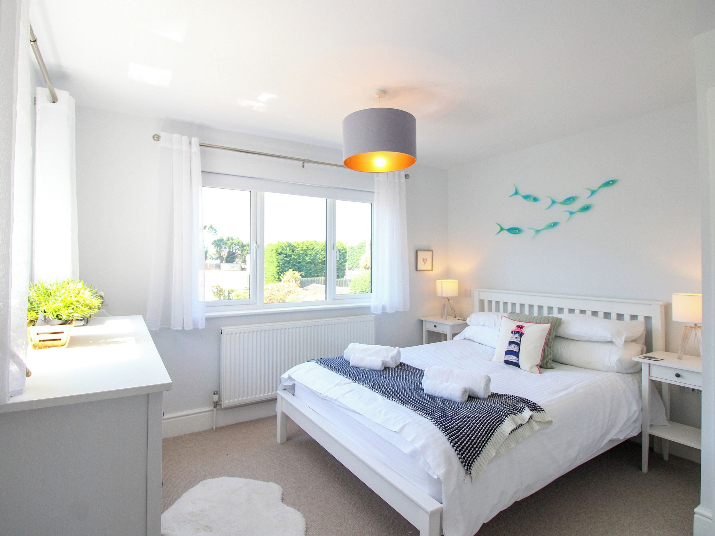 A bedroom with a large bed, bedside tables, a desk, a radiator, and a window with curtains.