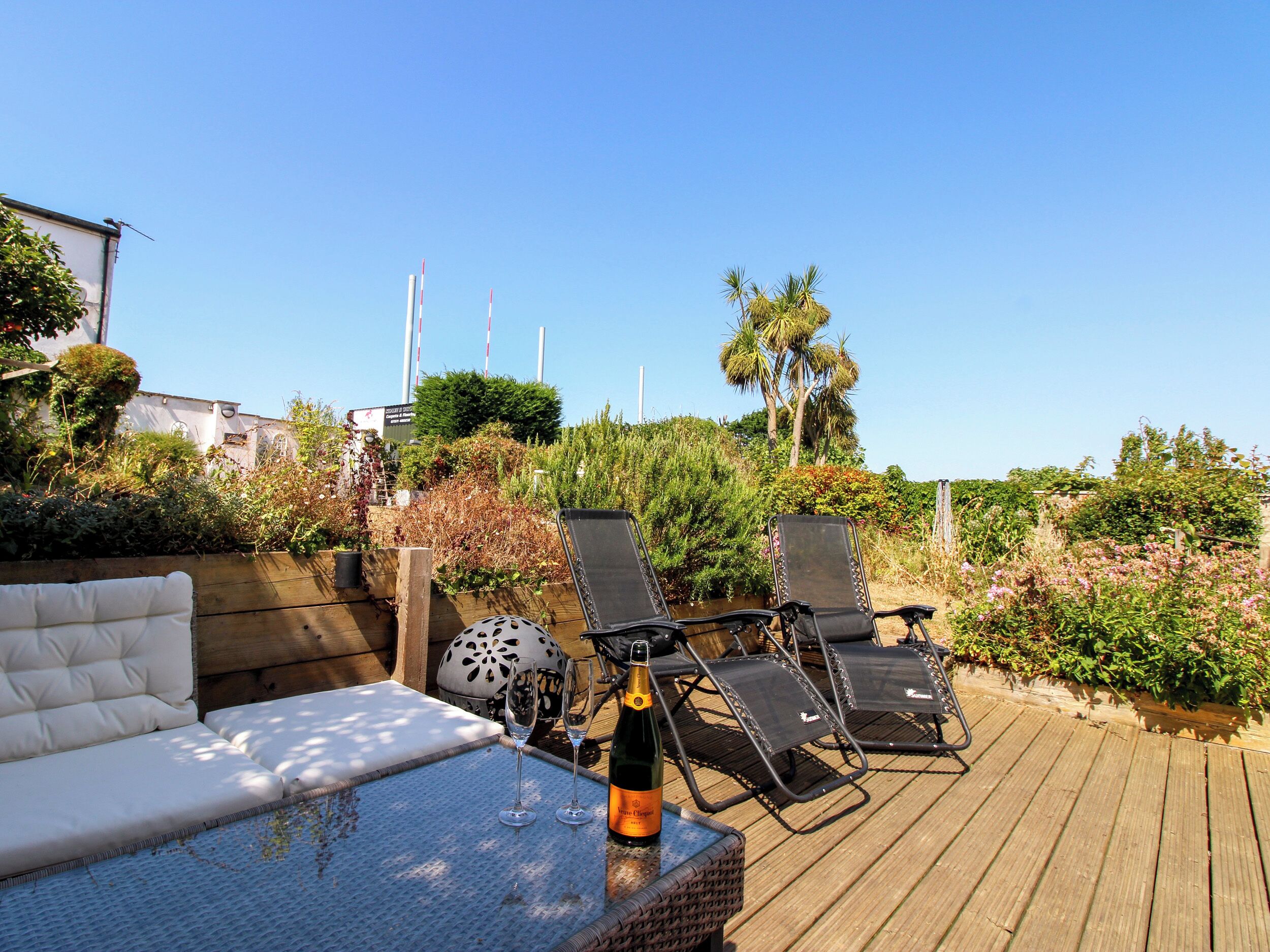 A deck with a sofa, lounge chairs, and a table with a bottle and glasses.