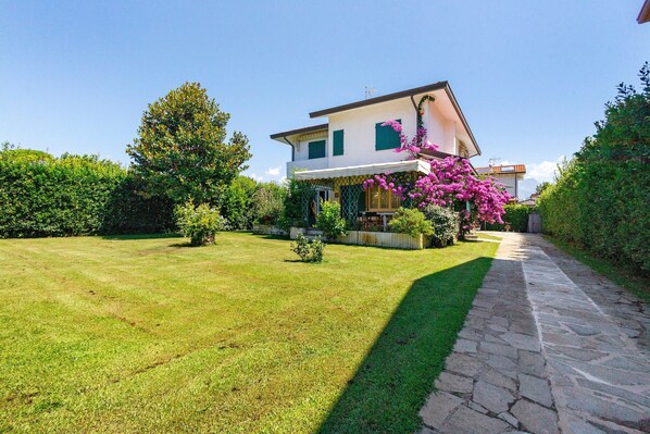Una casa a due piani con un vialetto in pietra che conduce all'ingresso, circondata da un prato curato e piante fiorite.