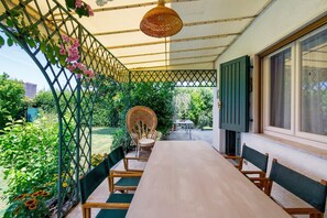 Una veranda riparata con tavolo e sedie in legno, una poltrona in vimini e un lampadario.