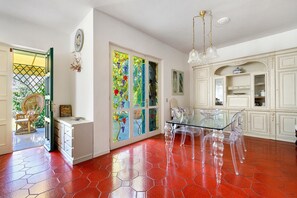 Una stanza con un tavolo da pranzo in vetro, sedie trasparenti, un armadietto bianco con ante in vetro e un pavimento in piastrelle rosse.