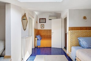 Un corridoio stretto con un letto alla destra, una porta in fondo e uno specchio alla sinistra.