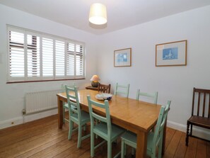 A dining room with a wooden table and six chairs, a window with blinds, a radiator, and two framed pictures on the wall. - Faraway (Ty Croes)