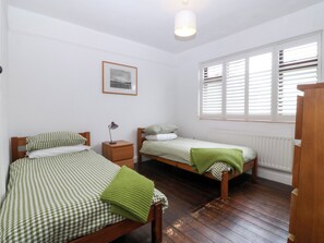 A room with two beds, a nightstand, a lamp, a framed picture on the wall, and a window with blinds. - Faraway (Ty Croes)