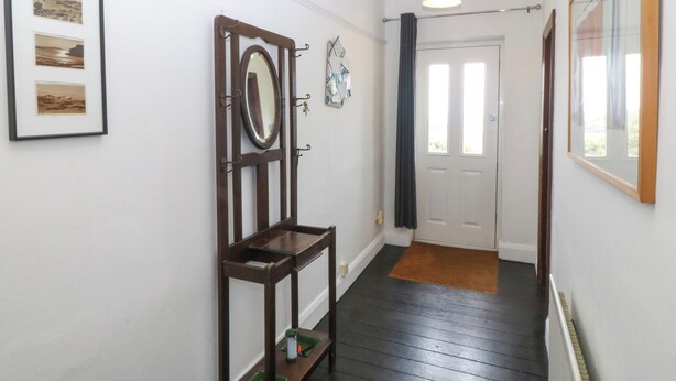 Een gang met een houten bankje, ingelijste foto's, een spiegel en een deur.