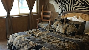 Un dormitorio con una cama grande, una silla, un tapiz con estampado de cebra y un cuadro en la pared.