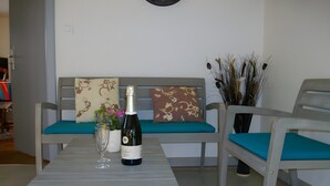 A room with a wooden table, a sofa with teal cushions, a decorative vase, and a bottle of wine. - Charming Cottage at the Foot of the Rock (Sewen)