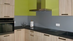 A modern kitchen with wooden cabinets, a black countertop, and a stainless steel range hood. - Charming Cottage at the Foot of the Rock (Sewen)