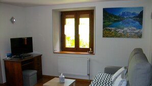 A living room with a TV, a window, a painting, and a sofa. - Charming Cottage at the Foot of the Rock (Sewen)
