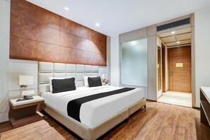 A modern hotel room with a large bed, a nightstand, a bedside table, a wooden floor, and a sliding door leading to a bathroom. - Super Townhouse Chhatarpur Near Metro Park (New Delhi)