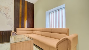 A room with a beige sofa, a glass coffee table, a wooden panel wall, and a window with vertical blinds. - Classic Ummed Palace (Mathura)