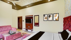 A hotel room with a bed, a sofa, a TV, and artwork on the wall. - Classic Ummed Palace (Mathura)