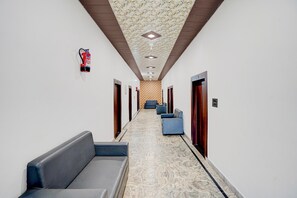 Ein Hotelgang mit Marmorboden, einem Feuerlöscher und einer Reihe blauer Stühle.
