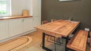A kitchen with white cabinets, a wooden table, and a bench. - Ghillie's Cottage (Killin)