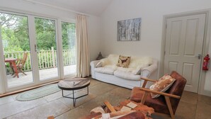A living room with a white sofa, leather chairs, a glass door leading to a balcony, and a fire extinguisher on the wall. - Ghillie's Cottage (Killin)