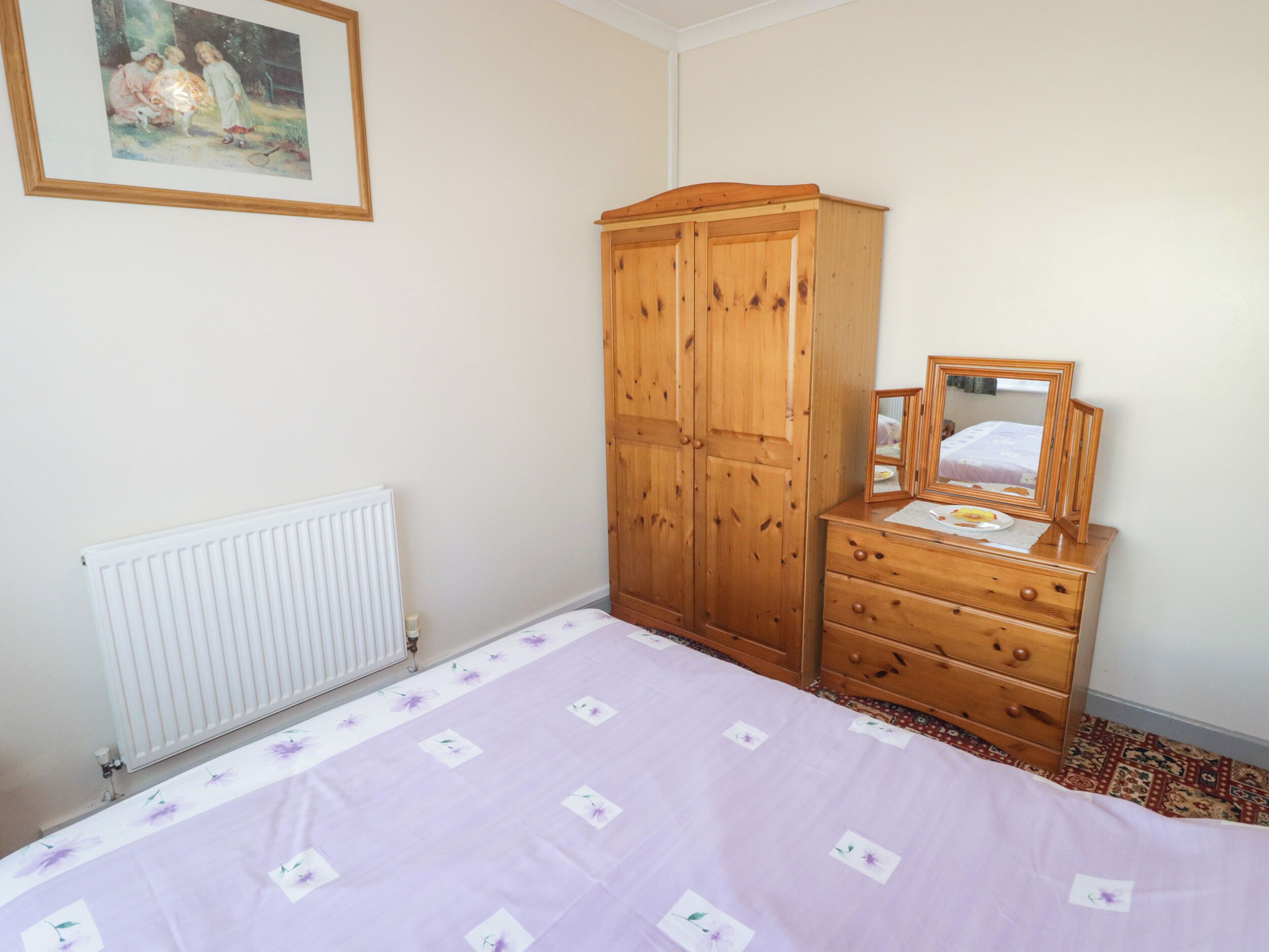 Quarto com cama, guarda-roupa de madeira, penteadeira, espelho e radiador.