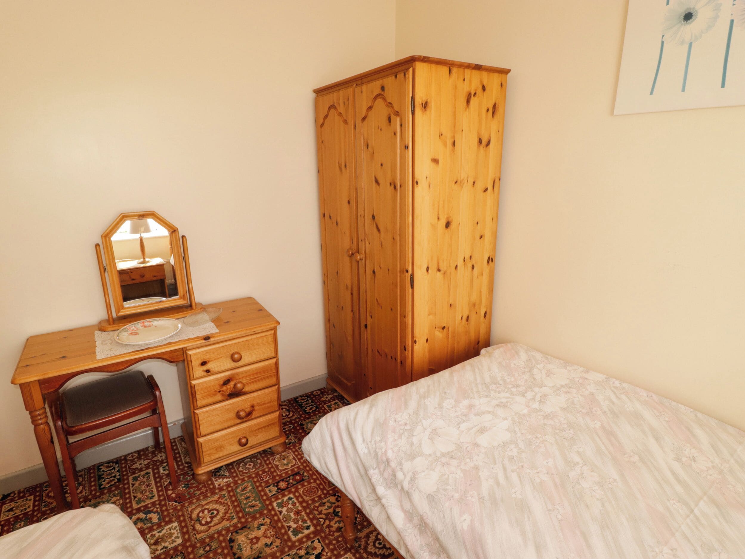 A bedroom with a wooden desk, a chair, a wardrobe, and a patterned carpet.