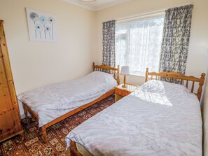 A bedroom with two single beds, a nightstand with a lamp, a wooden wardrobe, and a patterned carpet. - Cottage 3 (Tenby)