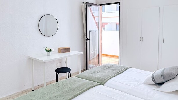 Une chambre à coucher comprenant un lit, un bureau, une chaise, un miroir et une porte-fenêtre coulissante donnant sur un espace extérieur.