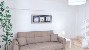 Un salon moderne avec un canapé beige, une plante en pot, un triptyque encadré et une table basse blanche.