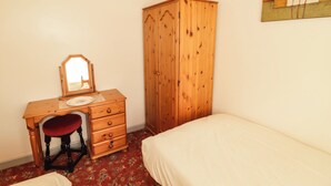 A bedroom with a wooden dresser, a mirror, a red chair, a bed, and a floral carpet. - Cottage 1 (Tenby)