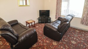 A living room with a sofa, a television, a small table, and a window with curtains. - Cottage 1 (Tenby)