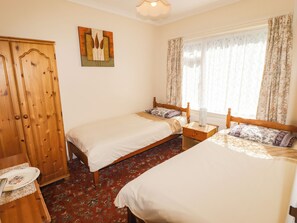 A bedroom with two single beds, a wooden wardrobe, a radiator, and a window with curtains. - Cottage 1 (Tenby)