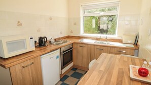 A compact kitchen with a microwave, kettle, sink, and a dishwasher. - Cottage 1 (Tenby)