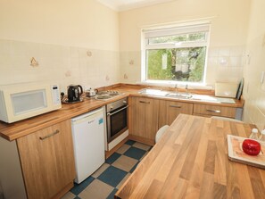A compact kitchen with a microwave, kettle, sink, and a dishwasher. - Cottage 1 (Tenby)